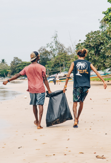 Two people holding a large garbage bag cleaning the beach